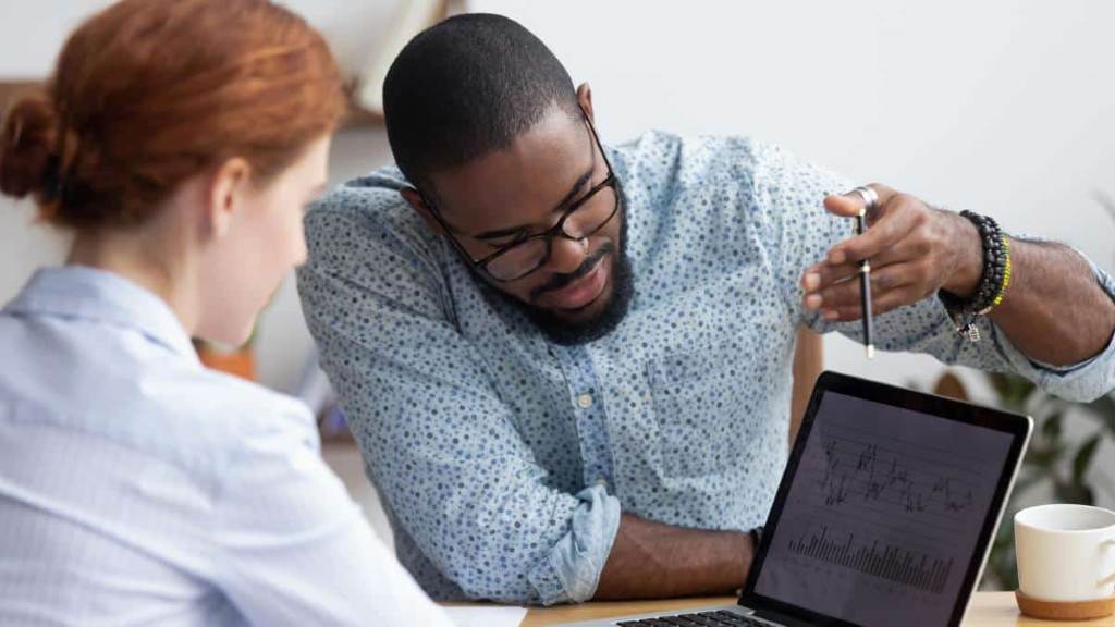 Mentor and apprentice discussing legal strategy at a desk with books and laptop.